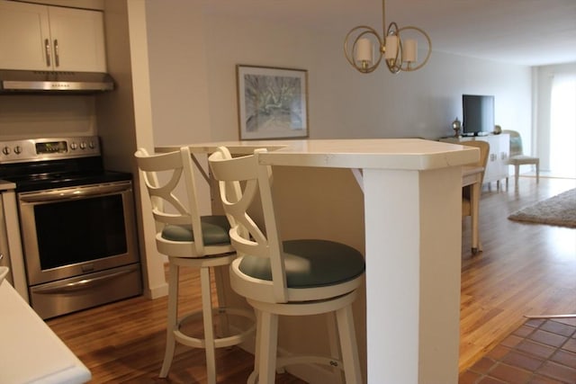 kitchen featuring electric range, a kitchen bar, light countertops, dark wood-style floors, and under cabinet range hood