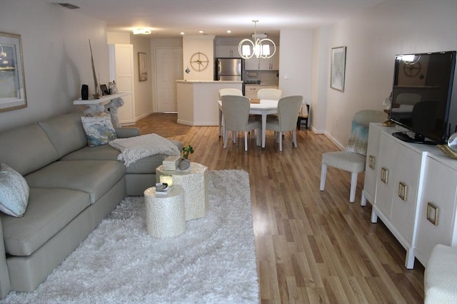 living area with baseboards, a notable chandelier, light wood-style flooring, and visible vents