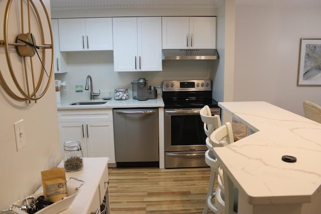 kitchen with a sink, light wood finished floors, stainless steel appliances, white cabinetry, and under cabinet range hood