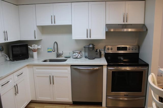 kitchen featuring under cabinet range hood, stainless steel appliances, white cabinets, and a sink