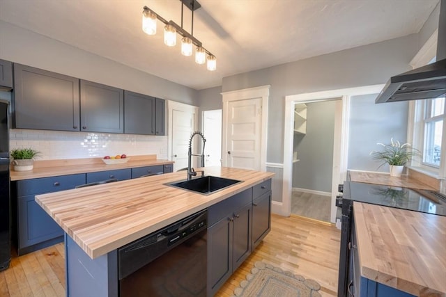 kitchen with sink, black dishwasher, hanging light fixtures, butcher block counters, and an island with sink