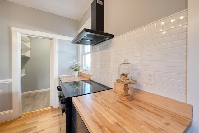 kitchen featuring wall chimney exhaust hood, stove, light hardwood / wood-style flooring, and wooden counters