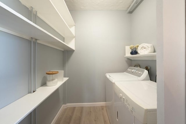 clothes washing area with washing machine and clothes dryer and light wood-type flooring