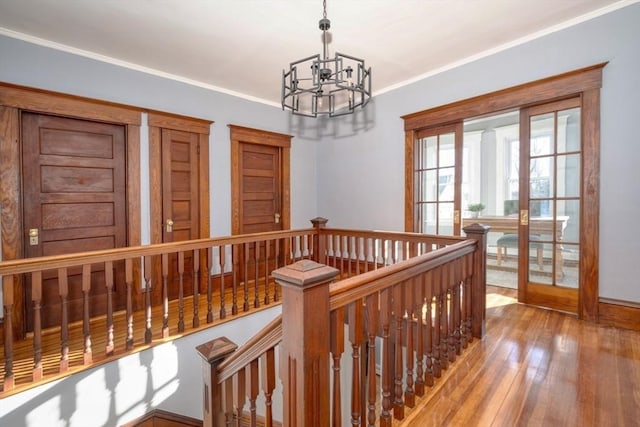 corridor with french doors, ornamental molding, a notable chandelier, and wood-type flooring