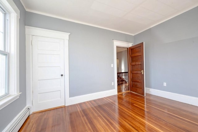 empty room with hardwood / wood-style floors, baseboard heating, and crown molding