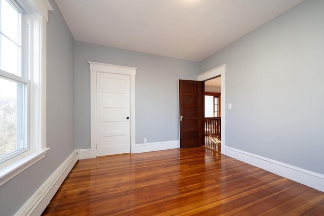 unfurnished bedroom with hardwood / wood-style floors and a baseboard heating unit