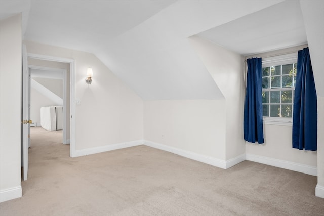 additional living space featuring vaulted ceiling and light colored carpet