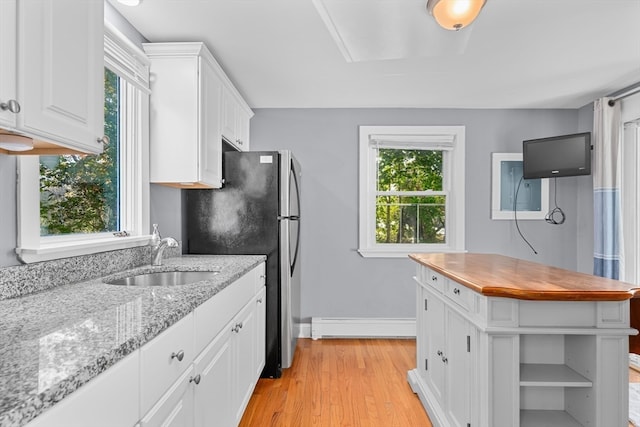 kitchen with light stone counters, white cabinetry, sink, light hardwood / wood-style floors, and baseboard heating