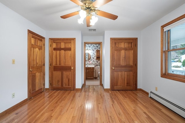 unfurnished bedroom with ceiling fan, a baseboard heating unit, connected bathroom, and light wood-type flooring