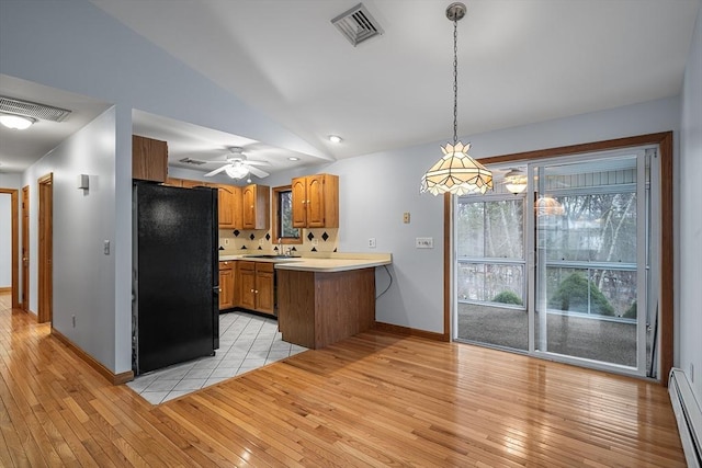 kitchen with decorative light fixtures, light hardwood / wood-style flooring, black refrigerator, baseboard heating, and kitchen peninsula