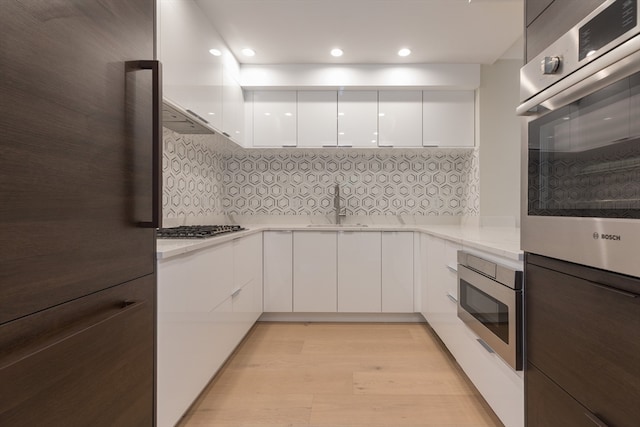 kitchen with light hardwood / wood-style flooring, white cabinets, appliances with stainless steel finishes, decorative backsplash, and sink