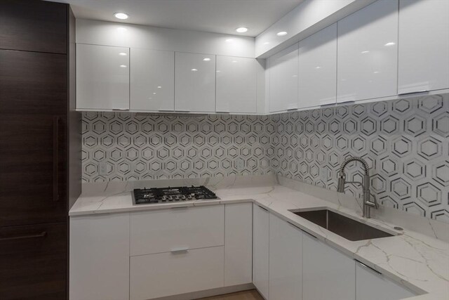 kitchen featuring stainless steel gas stovetop, white cabinetry, sink, decorative backsplash, and light stone counters