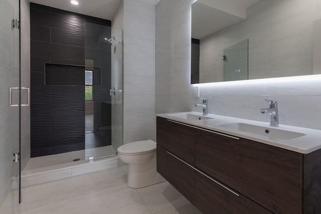 bathroom with a shower with shower door, toilet, tile walls, dual vanity, and tile patterned floors