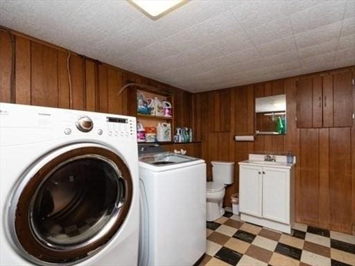 washroom with light floors, a sink, wooden walls, laundry area, and independent washer and dryer