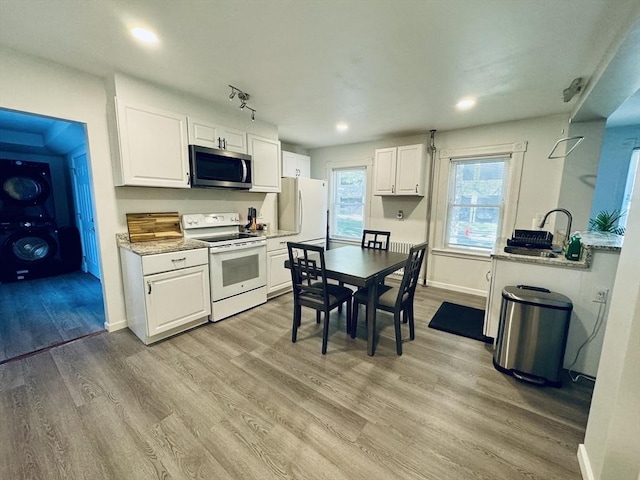 kitchen featuring stacked washer / dryer, white appliances, white cabinets, and light wood finished floors