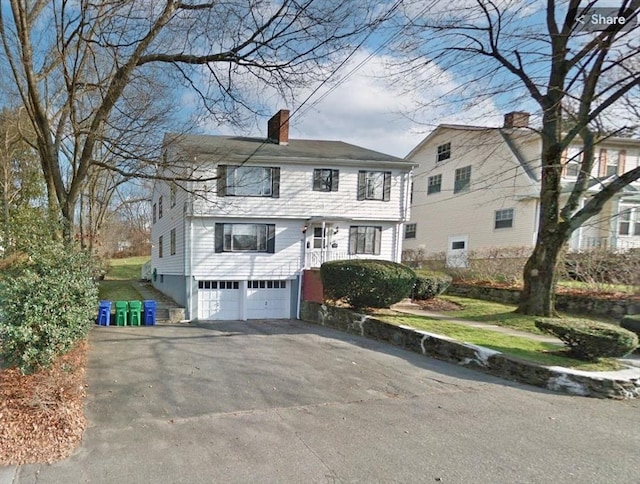 colonial home with aphalt driveway, a chimney, and an attached garage