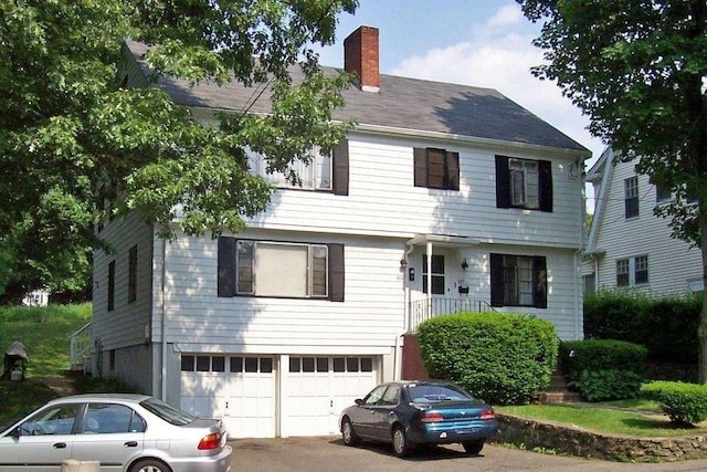 colonial inspired home with an attached garage, driveway, and a chimney