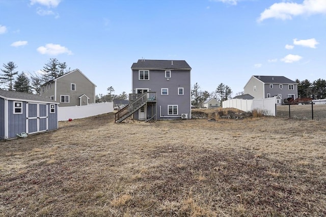 rear view of property with a storage unit, a fenced backyard, an outdoor structure, and stairs