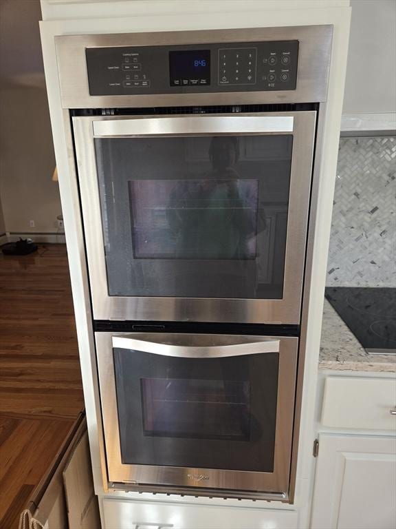 room details featuring backsplash, light stone counters, stainless steel double oven, stovetop, and white cabinets