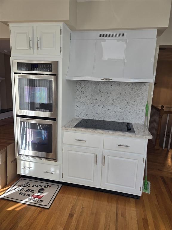 kitchen featuring black electric stovetop, backsplash, white cabinetry, and stainless steel double oven