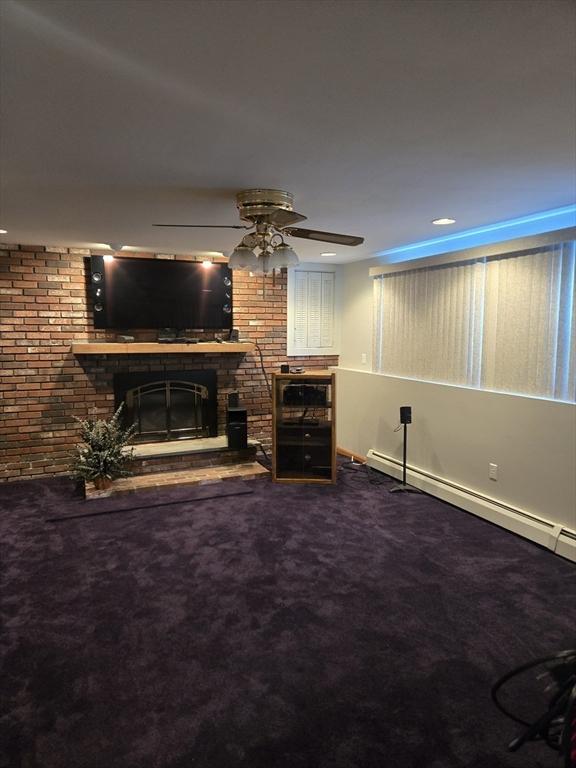 living room with carpet flooring, ceiling fan, a baseboard heating unit, and a brick fireplace