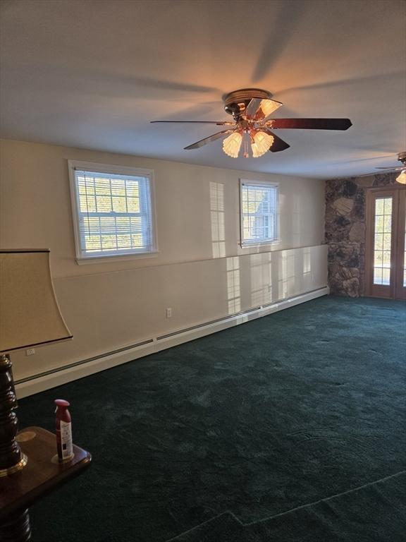 empty room with dark colored carpet, ceiling fan, and a baseboard heating unit