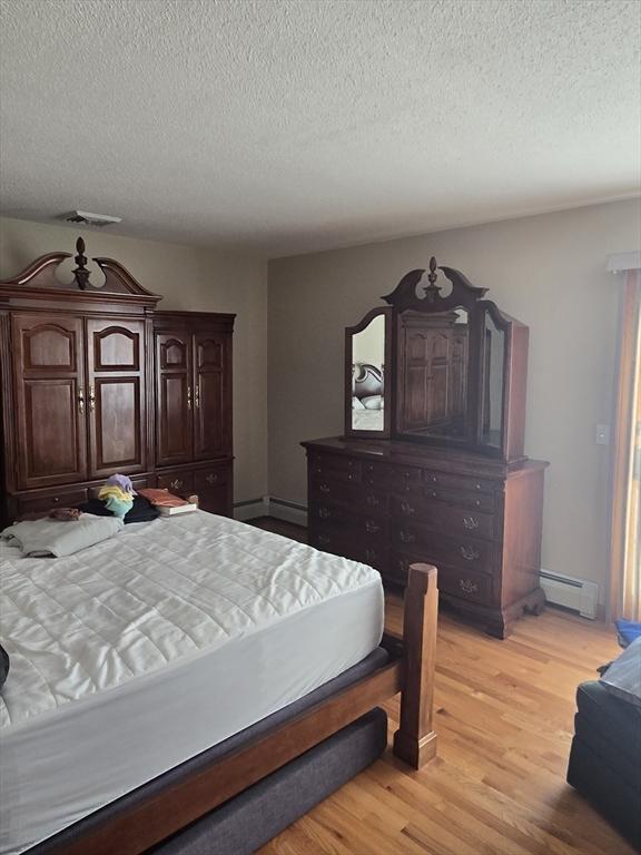 bedroom with baseboard heating, light hardwood / wood-style flooring, and a textured ceiling