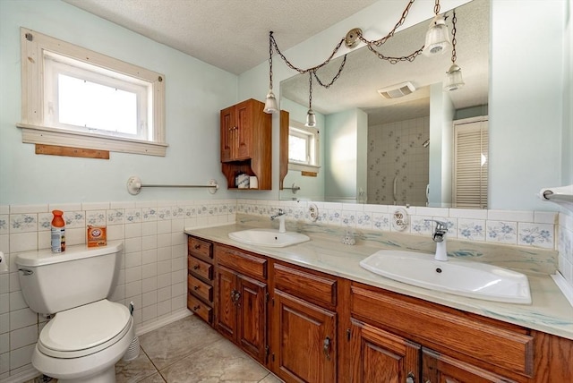 bathroom featuring tile patterned floors, a textured ceiling, toilet, vanity, and tile walls