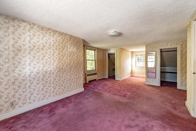 unfurnished bedroom with carpet flooring, radiator heating unit, a textured ceiling, and multiple windows