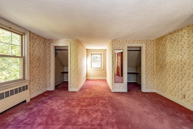 unfurnished bedroom with a spacious closet, radiator heating unit, carpet, and a textured ceiling