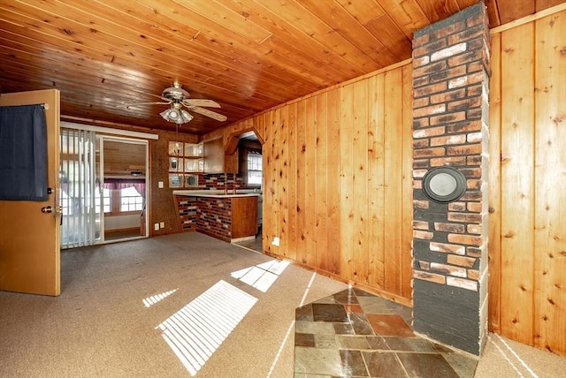 unfurnished living room with wooden walls, wooden ceiling, brick wall, and dark colored carpet