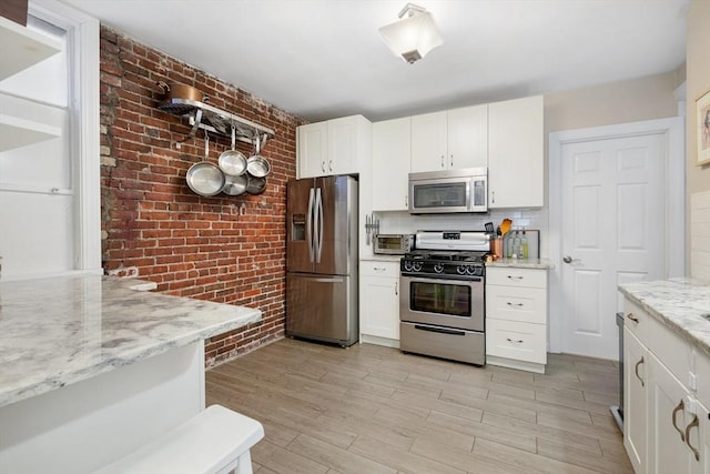37 Grove St Unit 2, Boston, MA 02114 - kitchen featuring stainless steel appliances, brick wall, white cabinets, light wood finished floors, and light stone counters