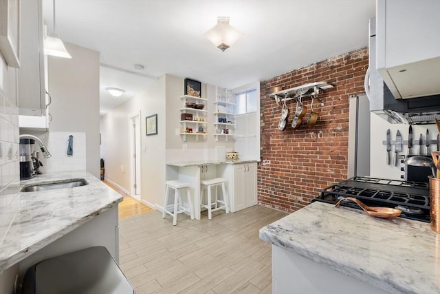37 Grove St Unit 2, Boston, MA 02114 - kitchen featuring a sink, brick wall, white cabinets, light wood-type flooring, and tasteful backsplash