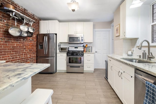 37 Grove St Unit 2, Boston, MA 02114 - kitchen featuring stainless steel appliances, a sink, brick wall, white cabinets, and light stone counters