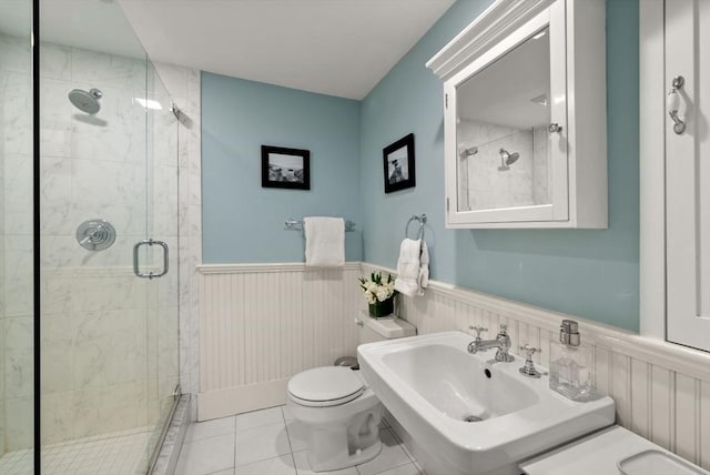 full bath with tile patterned floors, a wainscoted wall, toilet, a stall shower, and a sink