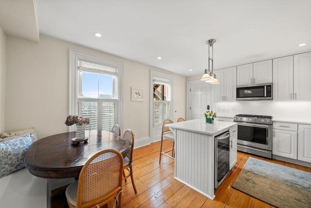 kitchen with beverage cooler, light countertops, appliances with stainless steel finishes, light wood-style floors, and white cabinets