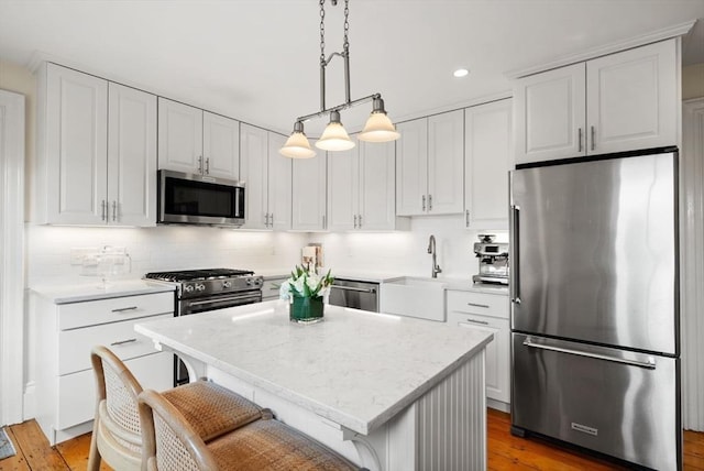 kitchen with a sink, a kitchen island, backsplash, white cabinetry, and appliances with stainless steel finishes