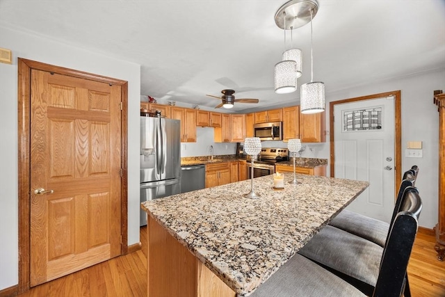 kitchen with a kitchen island, appliances with stainless steel finishes, light wood-type flooring, and decorative light fixtures