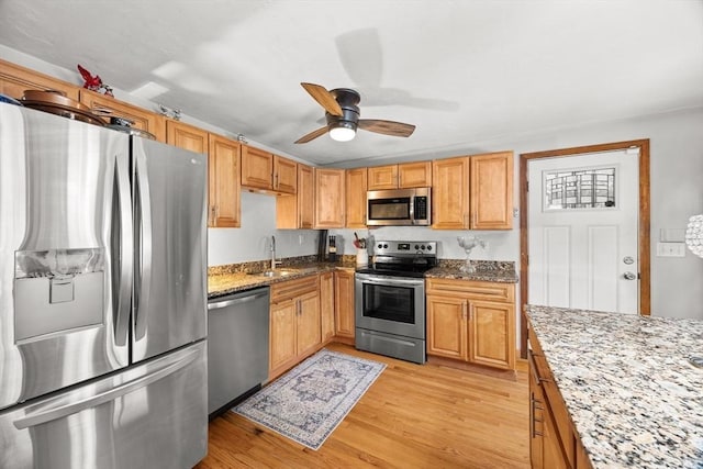 kitchen with sink, ceiling fan, stainless steel appliances, light stone counters, and light hardwood / wood-style floors