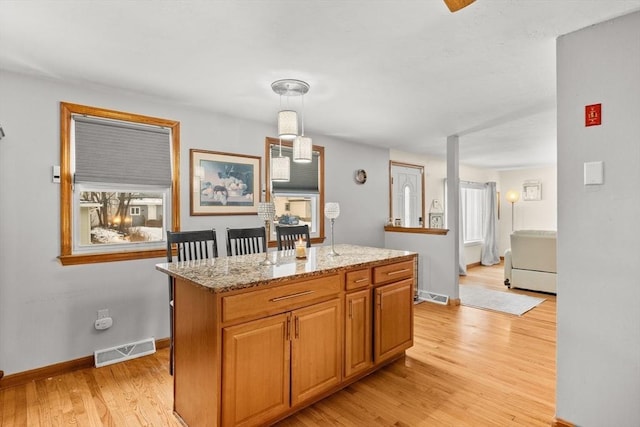 kitchen featuring pendant lighting, a center island, light stone counters, and light wood-type flooring