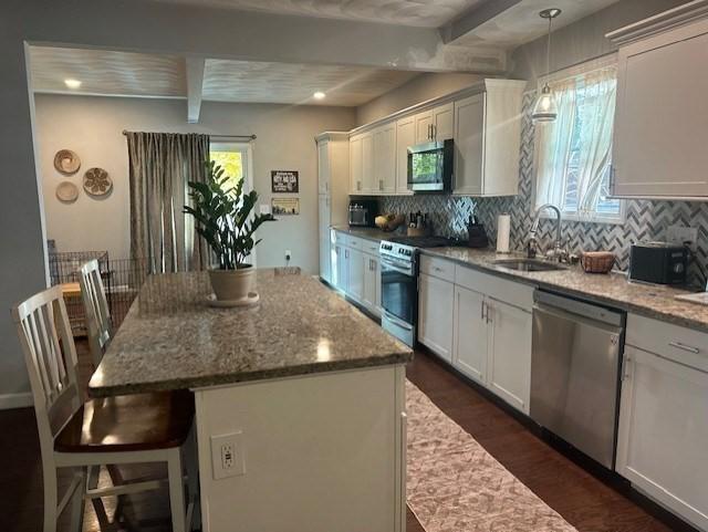 kitchen featuring a center island, sink, beam ceiling, light stone counters, and stainless steel appliances