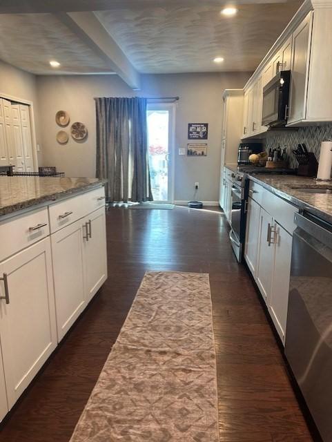 kitchen with appliances with stainless steel finishes, light stone counters, beamed ceiling, white cabinets, and dark hardwood / wood-style floors