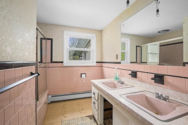 full bathroom with a sink, baseboard heating, tile walls, wood finished floors, and wainscoting