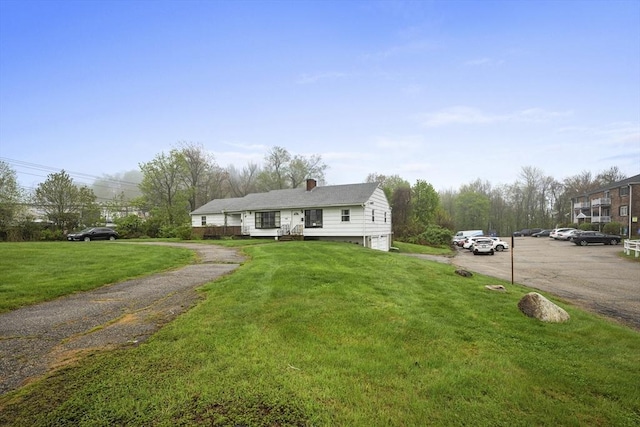 single story home featuring uncovered parking, a front lawn, and a chimney