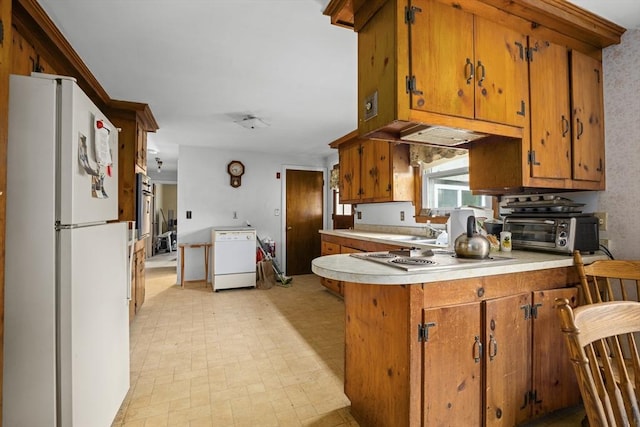 kitchen with freestanding refrigerator, brown cabinets, light countertops, a peninsula, and stovetop