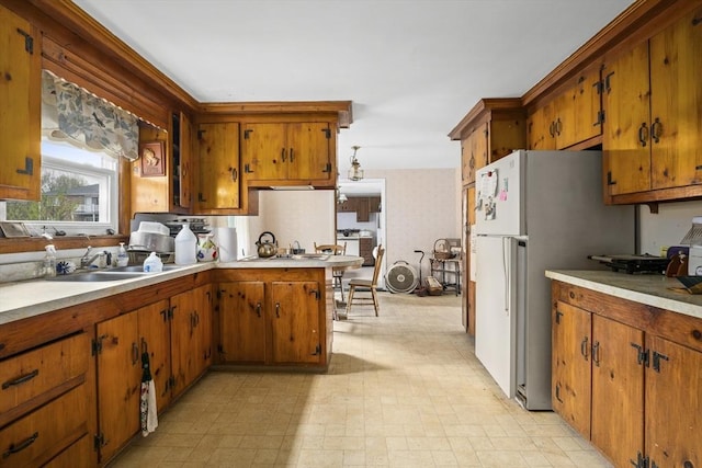 kitchen featuring brown cabinets, light countertops, a sink, and a peninsula