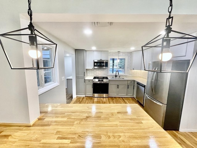 kitchen with backsplash, gray cabinets, light hardwood / wood-style floors, sink, and appliances with stainless steel finishes