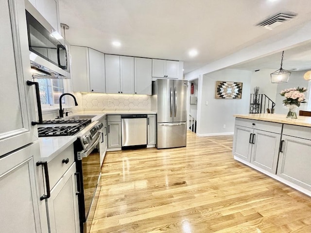 kitchen featuring pendant lighting, appliances with stainless steel finishes, white cabinetry, sink, and light wood-type flooring