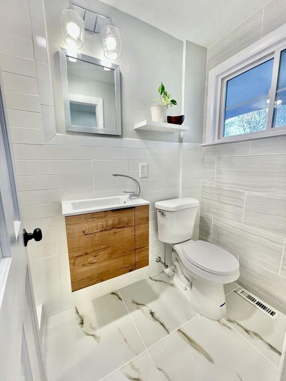 bathroom with toilet, vanity, and tile walls