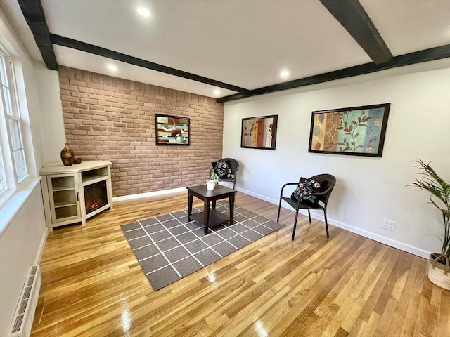 sitting room featuring light wood-type flooring, brick wall, and beam ceiling